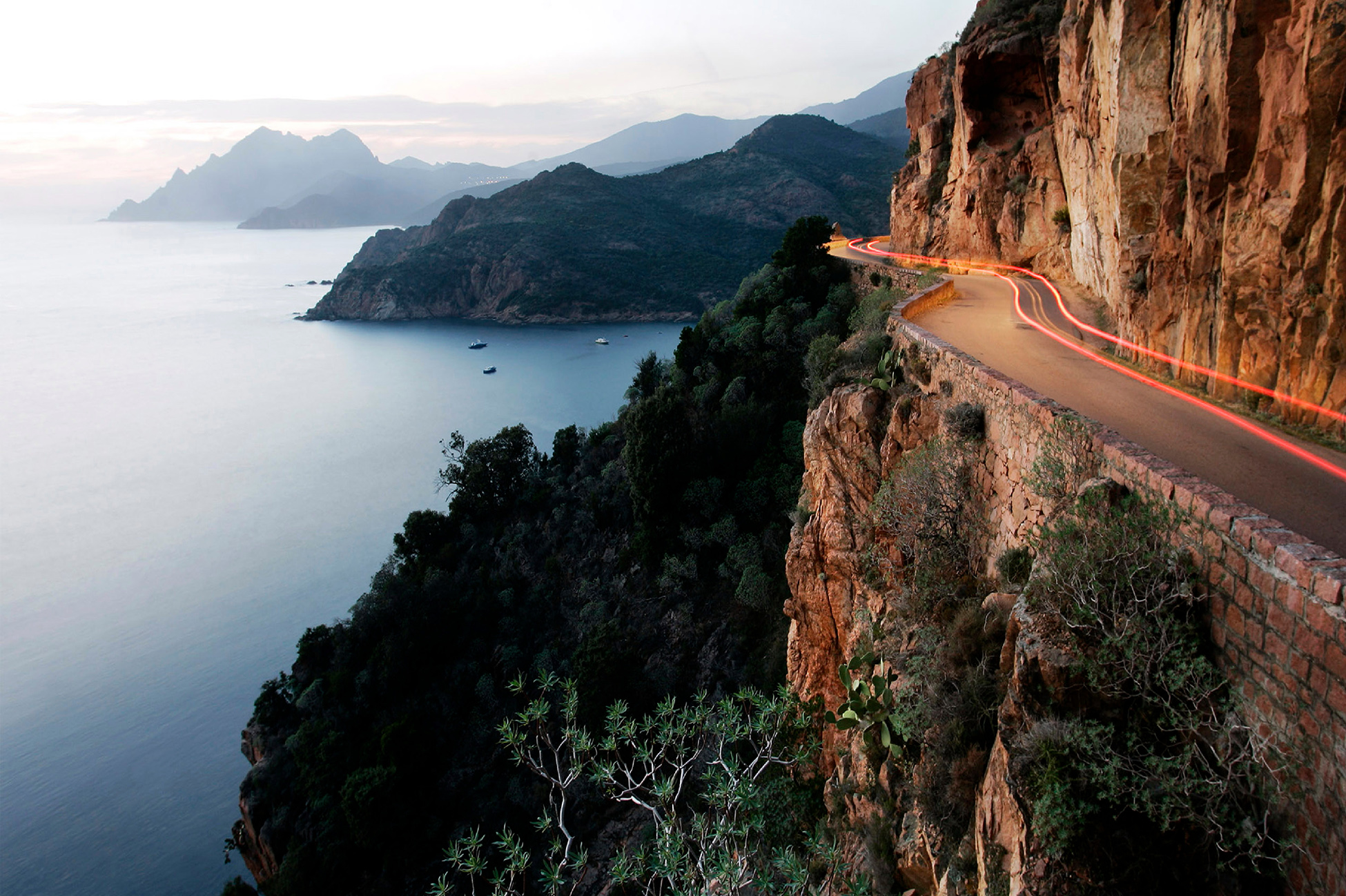A car hugs the cliffes at Sundown overlooking the Mediterranean Sea just outside the village of Porto, Korsika, France