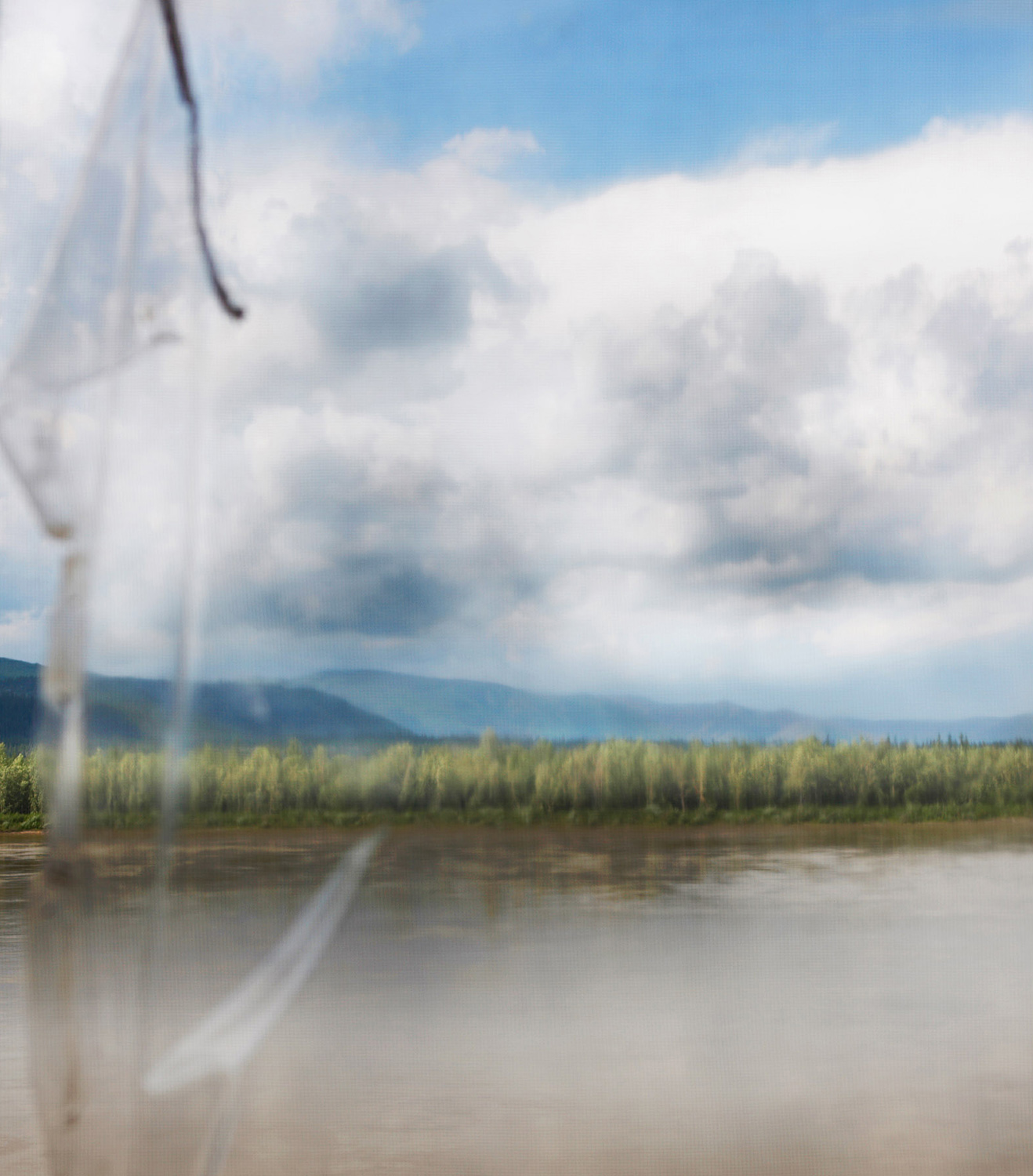 Ein Blick aus dem Fenster einer Fischerhütte mit Blick auf den Yukon River. Die Hütten werden während der Lachssaison genutzt, bleiben aber ansonsten leer. Der Yukon River fließt von seiner Quelle in Britisch-Kolumbien (Kanada) durch das Yukon Territory, bevor er die Grenze zu Alaska überquert und in etwa 3000 km Entfernung in das Beringmeer mündet. Der Fluss hat eine geschichtsträchtige Goldrausch-Geschichte und ist eine der schönsten Wasserstraßen der Welt. Er ist ein fantastischer Spielplatz für SUPs, Kajakfahrer, Kanufahrer, Jäger und Fischer.