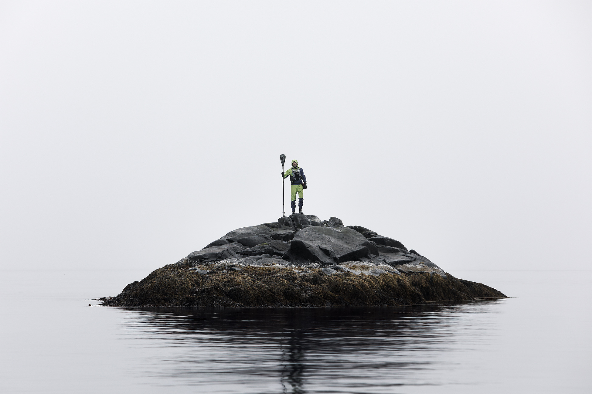 Graphic creative photo of a lone Stand Up Paddler standing on a isolated rock formation in the middle of the sea, Norway