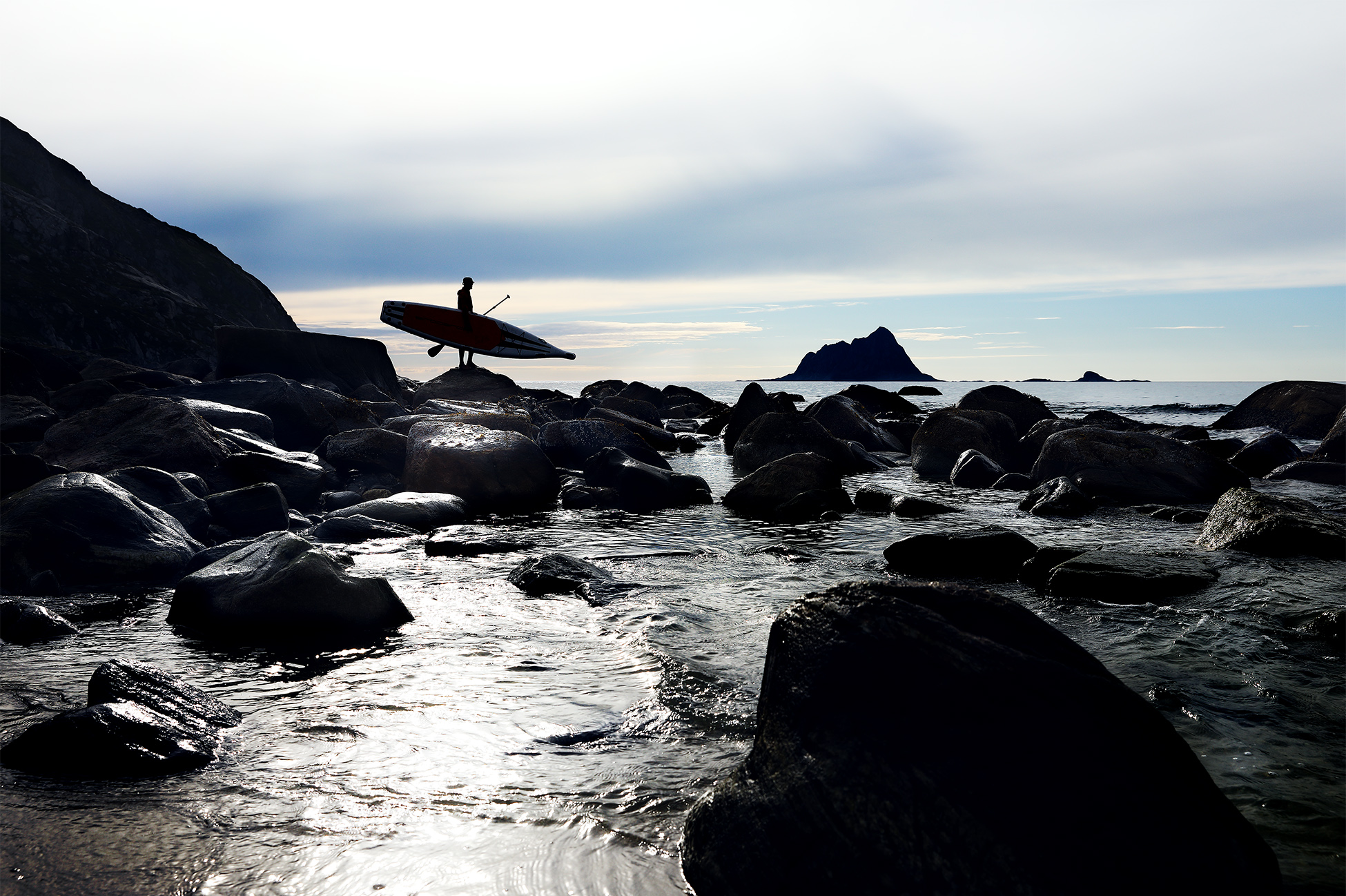 A lone Stand Up Paddler surveys the surroundings for a good place to put into the water in Norway beneath the endless Midnight Sun.