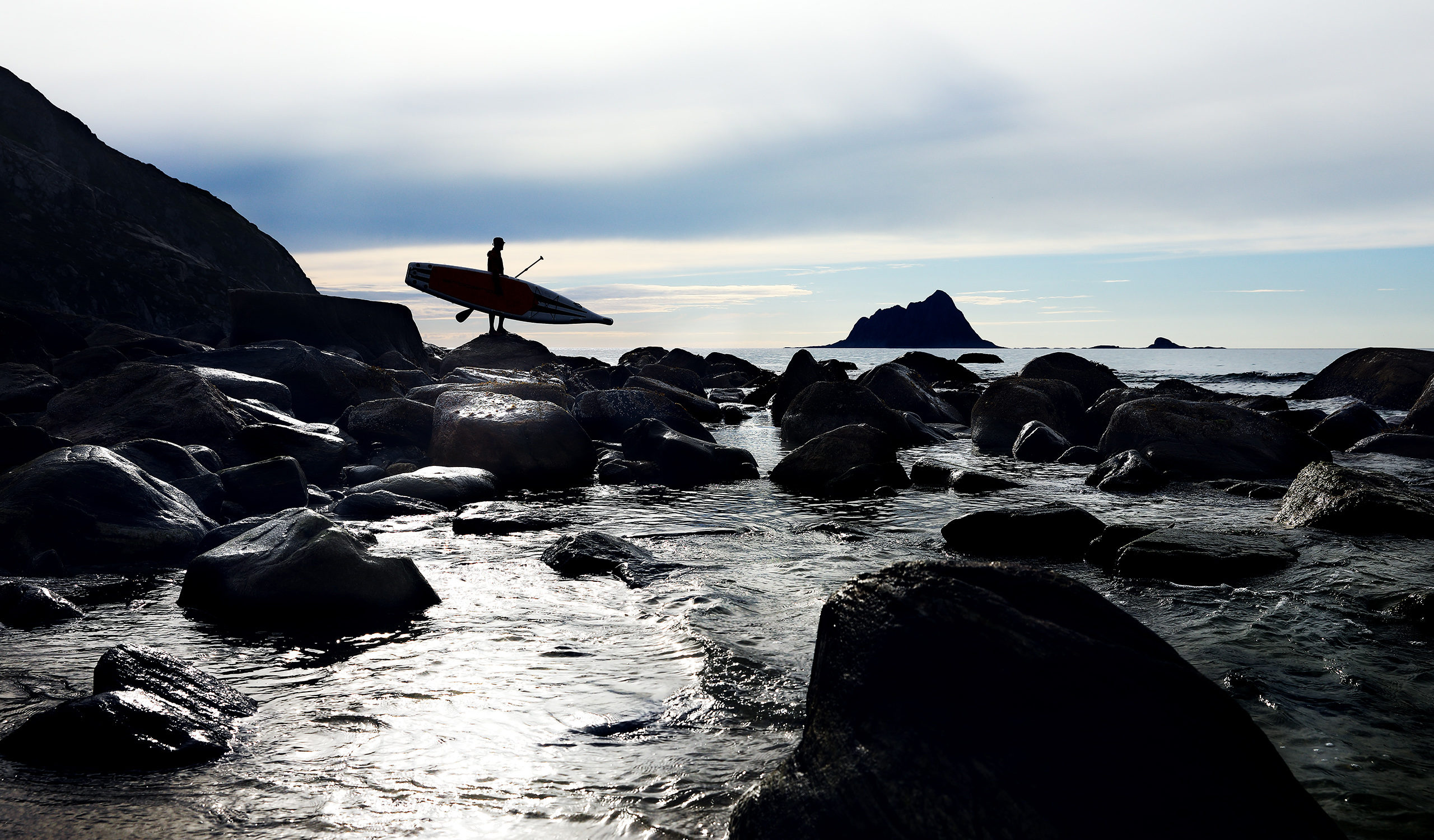 Ein Stehpaddler schaut in der norwegischen Arktis rund um die Insel Rebbenesoya aufs Meer hinaus. Das mystische Wetter der norwegischen Arktis bietet ein emotionales Ambiente für jeden, der bereit ist, sich in die Ferne zu wagen. Planetvisible hat eine 14-tägige Reise in die nördliche norwegische Arktis unternommen, um die Fähigkeit der Bretter zu testen, den Wellengang des offenen Ozeans mit mehr als 130 kg an Bord zu überstehen. Fotografie von Justin Hession Fotografie