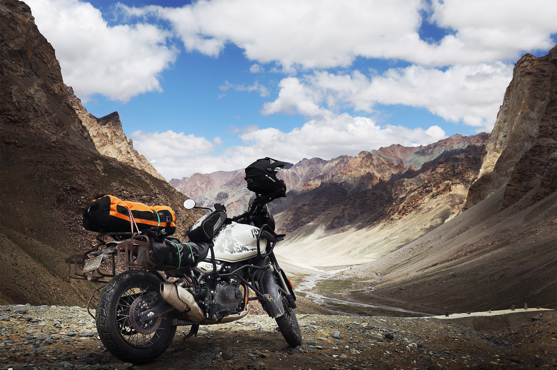 Motorcyclist riding on a mountain road in Ladakh with snow-capped peaks and barren high-altitude desert terrain.